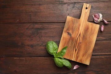 Cutting board, basil and garlic on wooden table, flat lay. Space for text