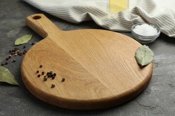 Cutting board, pepper and bay leaves on grey table. Space for text