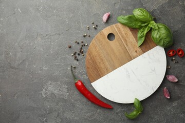 Cutting board, basil, pepper, chili peppers and garlic on grey table, flat lay. Space for text
