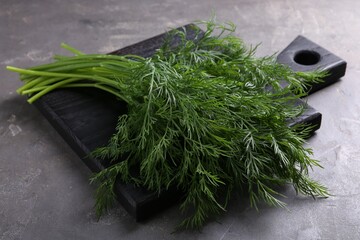 Board with sprigs of fresh dill on grey textured table, closeup