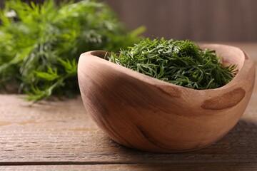 Fresh cut dill in bowl on wooden table, closeup