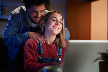 Loving man standing behind woman working on laptop at home. Supporting spouse at online business...