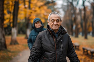 Content senior man enjoys a peaceful walk in an autumn park with a woman in the background