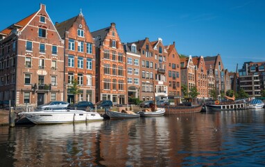 Red-brick waterfront buildings line a canal with boats under a clear blue sky.