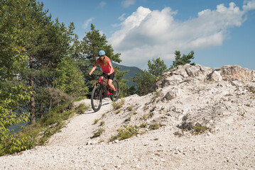 Female biker riding an electric mountain bike on a fine white stone trail, surrounded by fantastic...