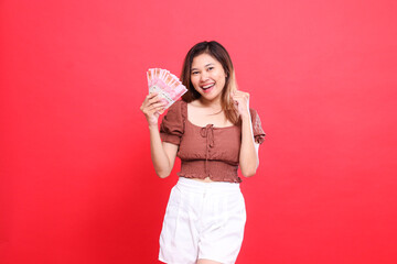 gesture of a cheerful indonesia woman clenching her fist successfully while holding rupiah money...