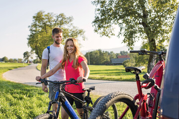 Obraz premium Young man is unloading electric mountain bikes, for himself and his girlfriend, lifting them from the hitch rack on the vehicle.