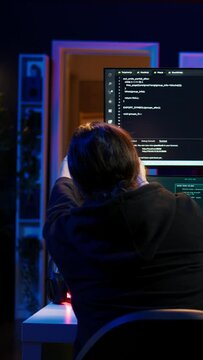 Vertical video Dangerous hacker writing lines of code on PC from secret apartment, trying to get past security systems. Evil software developer building scripts that can hack devices, camera B