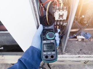 Checking the electric current in the HVAC air conditioning electrical system using an ammeter by an electrician. the enginer wear blue gloves checking electrical system on hvac.