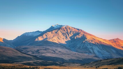A mountain range bathed in the golden light of sunrise, with a clear sky gradually transitioning to blue.