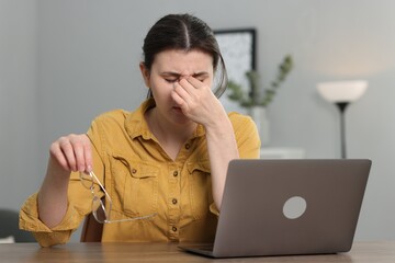 Overwhelmed woman sitting with laptop at table indoors