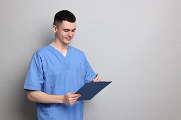 Portrait of smiling medical assistant with clipboard on grey background. Space for text