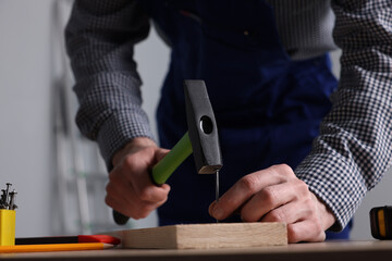 Professional repairman hammering nail into board at wooden table indoors, closeup