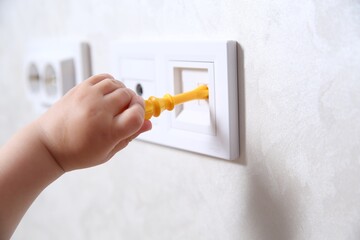 Little child playing with toy screwdriver and electrical socket indoors, closeup. Dangerous...