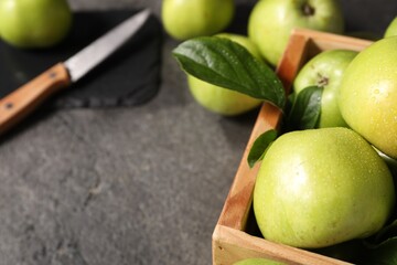 Ripe green apples with water drops in crate on grey table, closeup