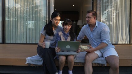 Father, mother and daughter focus laptop at terrace with garden view outside house. Parent use...