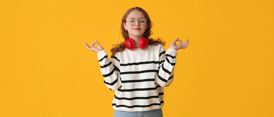 Portrait of relaxed young woman with headphones meditating on yellow background