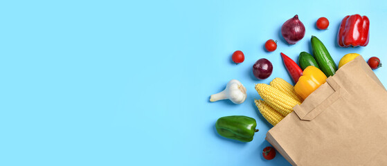 Paper bag with fresh vegetables on blue background