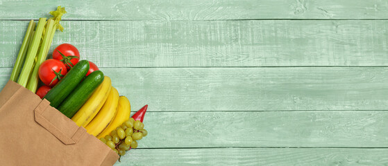 Paper bag with fresh vegetables and fruits on green wooden background