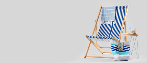 Deckchair with beach accessories, cocktail and coral on stool against grey background