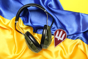 Badge with trident and military headphones on crumpled flag of Ukraine
