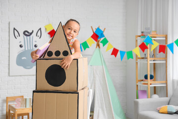 Cute little girl with adventure book and cardboard rocket at home