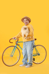 Senior woman with Pomeranian dog and bicycle on yellow background