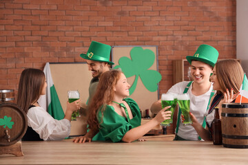 Group of young friends with beer celebrating St. Patrick's Day at table in pub