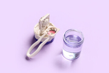Cleaning case for contact lenses and tweezers on lilac background