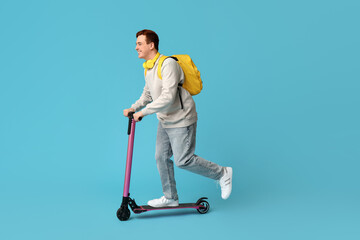 Happy young man riding modern electric kick scooter on blue background
