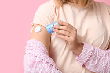 Woman with glucose sensor for measuring blood sugar level and applicator on pink background,...