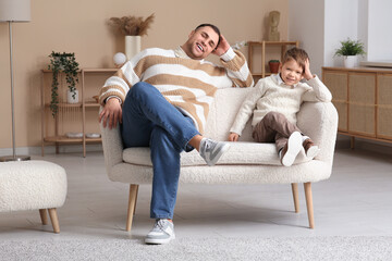 Happy father and his little son sitting on sofa at home