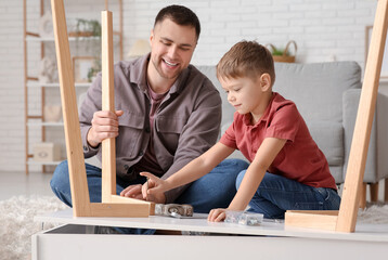 Happy father and his little son assembling table at home