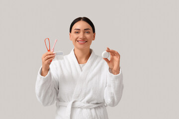 Beautiful young happy woman in bathrobe with supplies for oral hygiene on grey background