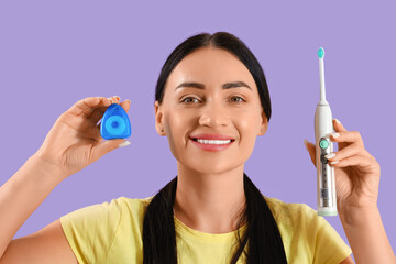 Beautiful young happy woman with dental floss and electric toothbrush on purple background