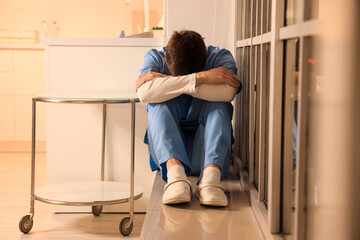 Stressed male nurse sitting on windowsill at hospital in evening
