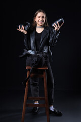 Portrait of stylish female photographer with modern camera and lens on black background