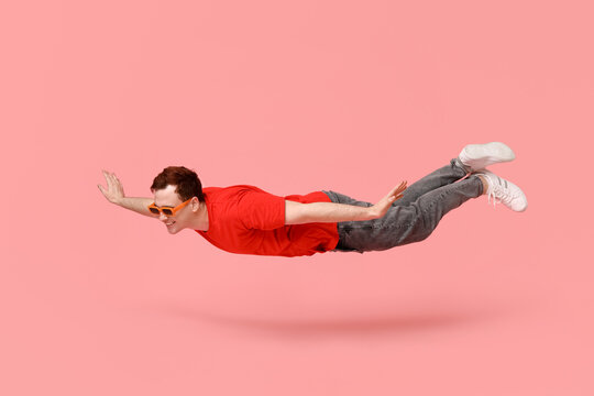 Joyful young man in sunglasses flying on pink background