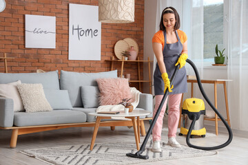 Young woman cleaning rug with vacuum cleaner at home