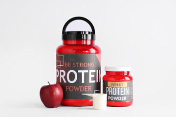Bottles with protein powder and apple on light background