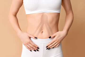 Young woman with physio tape applied on her belly against color background, closeup