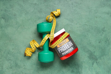 Bottle of protein powder, dumbbell and measuring tape on color background