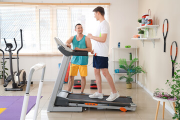 Male coach with young man training on treadmill in gym