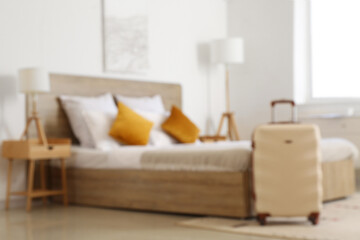 Blurred view of modern hotel room with suitcase near bed