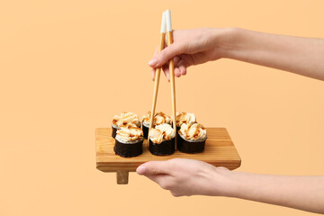 Hands with tasty maki rolls and chopsticks on beige background