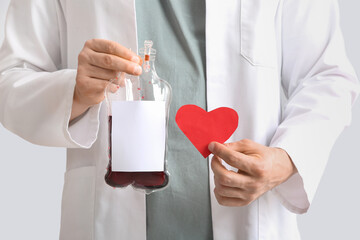 Doctor with blood pack and paper heart on grey background, closeup. Blood donation concept