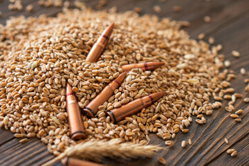 Wheat grains are spread across a wooden table, interspersed with several metal bullet shells. The...