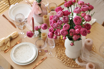 Beautiful table setting with pink roses and candles for wedding celebration in room, closeup