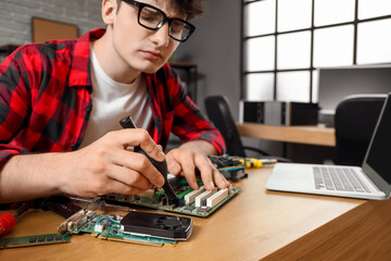 Fototapeta premium Male technician repairing computer board at table in service center, closeup