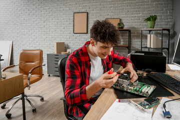 Male technician with screwdriver repairing computer board at table in service center